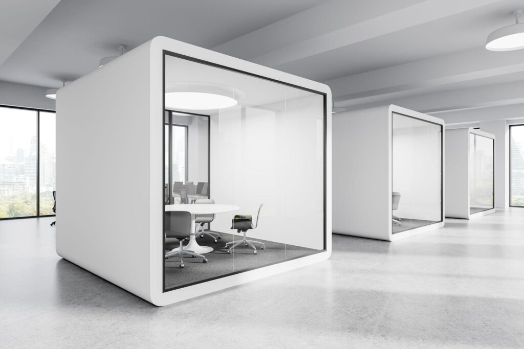 Modern glass-enclosed meeting pods with chairs and tables in a bright, minimalist office space.